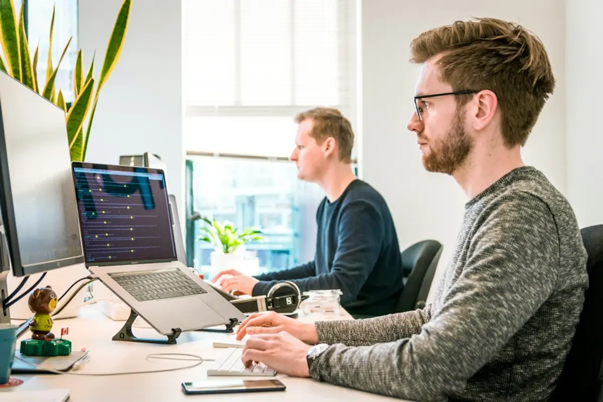 Person checking dating app photo policies on a phone next to a laptop